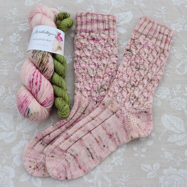 Rosa gestrickte Damensocken mit wabenartigem Schaftmuster neben zwei Garnsträngen in Rosa und Grün