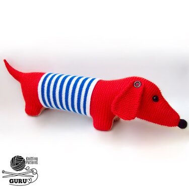 Red knitted dachshund toy with blue-and-white striped midsection, black button eyes and black nose on a white background.