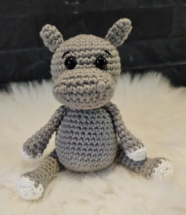 Nahaufnahme eines sitzenden gehäkelten Nilpferds mit sichtbaren Maschen und weißen Pfoten