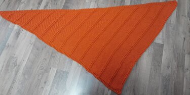 Gestricktes orangenes Dreieckstuch mit diagonalem Rippenmuster auf hellem Holzboden