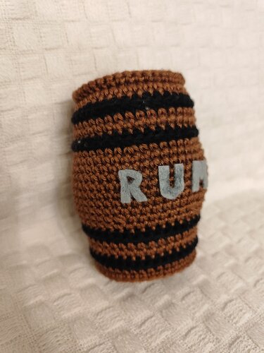 Braunes gehäkeltes Amigurumi-Fass mit schwarzen Streifen und applizierten Buchstaben RUM