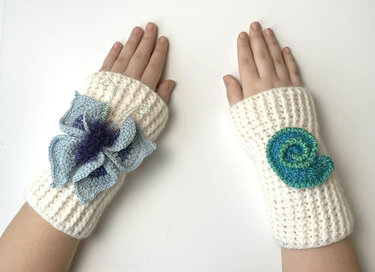 Fingerlose cremefarbene gehäkelte Handstulpen für Kinder, links mit blauer Blüte, rechts mit grüner Spirale