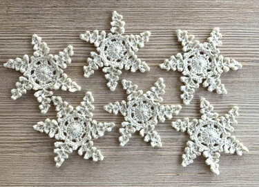 Sechs gehäkelte cremefarbene Schneeflocken auf Holzuntergrund