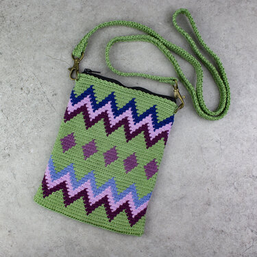 Grüne gehäkelte Umhängetasche mit Zickzack- und Rautenmuster in Lila und Blau auf grauem Untergrund