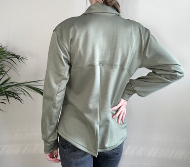 Rückansicht einer Person in salbeigrüner Damenjacke mit Kragen, mittiger Rückennaht und geteiltem Saum