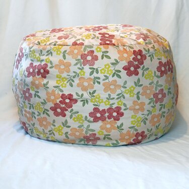 Runder Pouf mit sichtbaren Nähten und geblümtem Stoffbezug