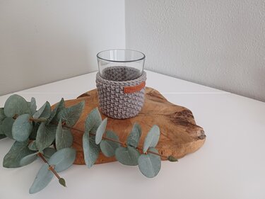 Klares Glas mit grauem gehäkeltem Überzug auf Holzbrett neben Eukalyptuszweig