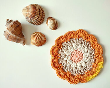 small scalloped-edge crochet coaster in orange and beige styled with seashells