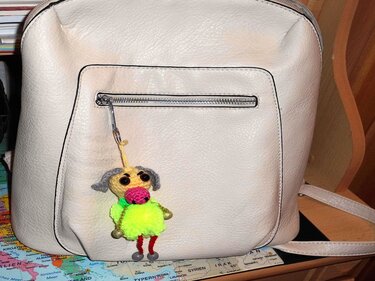 Gehäkelter Amigurumi-Schlüsselanhänger mit neongrüner Bommel, pinker Schnauze und grauen Ohren an hellem Rucksack.