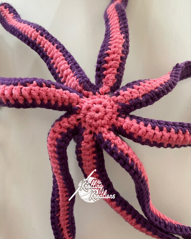 Top-down view of a crocheted octopus amigurumi with pink and purple striped tentacles.