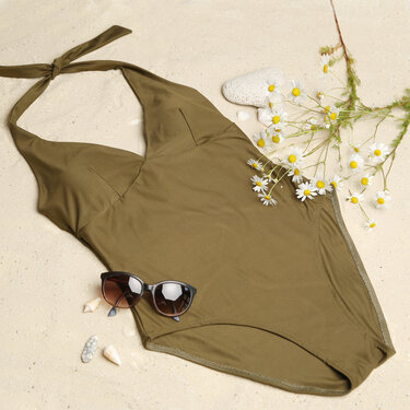 Dunkelgrüner Neckholder-Badeanzug auf Sand mit Sonnenbrille und Gänseblümchen