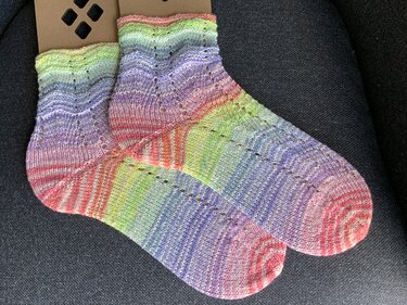 Paar handgestrickter Pastell-Socken mit Lochmuster auf dunklem Untergrund