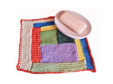 Bunter gehäkelter Waschlappen im Patchwork‑Muster mit Seifenschale und Seife auf weißem Hintergrund