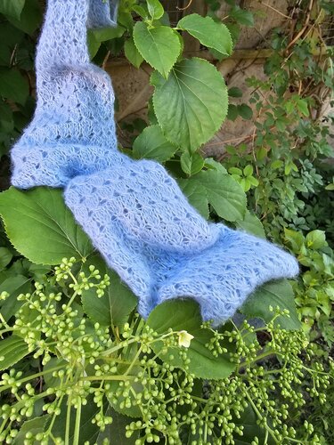 Hellblaues gestricktes Dreieckstuch mit Lochmuster auf grünen Blättern