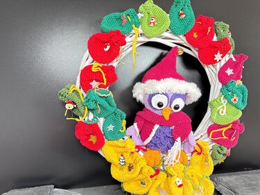Weißer Kranz mit gehäkelter Eule in der Mitte und bunten gehäkelten Adventssäckchen ringsum