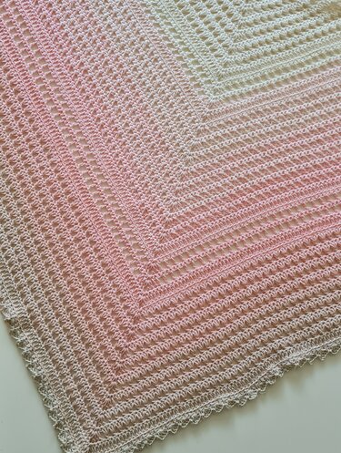 Detail eines gehäkelten Dreieckstuchs in Pastellrosa bis Creme mit Lochmuster und Muschelrand