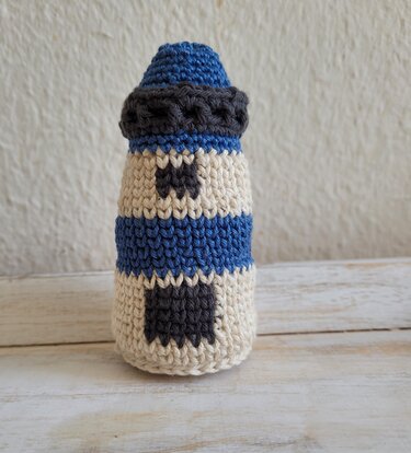 Handgehäkelter Amigurumi-Leuchtturm mit blauen und beigen Streifen auf hellem Holzuntergrund