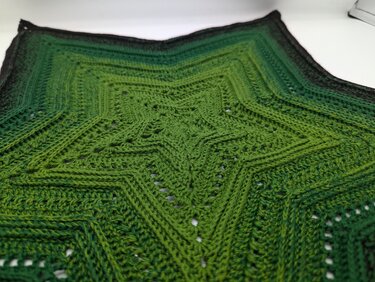 Gehäkeltes sternförmiges Deckchen in verschiedenen Grüntönen mit sichtbaren Rippenreihen