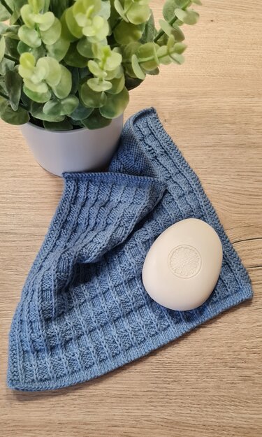 Gestrickter blauer Topflappen mit strukturierter Oberfläche neben ovaler Seife und Topfpflanze
