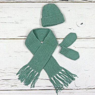 Gestricktes Baby-Set mit Mütze, Fransen-Schal und Fäustlingen auf hellen Holzplanken