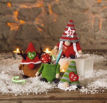 Nahaufnahme mehrerer gehäkelter Amigurumi‑Wichtel mit nummerierten Applikationen, Kerzen und Kunstschnee