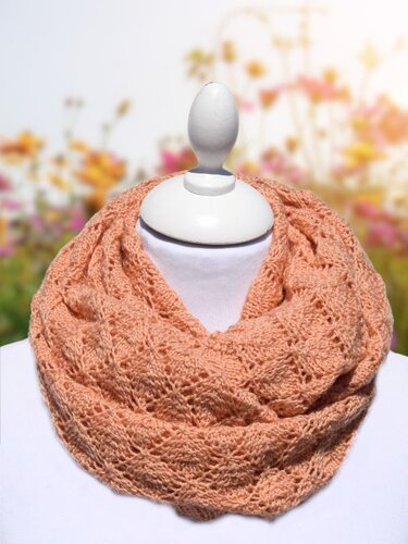 Apricotfarbener gestrickter Loop mit Ajourmuster auf Schaufensterpuppe vor unscharfem Blumenhintergrund