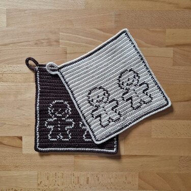 Gehäkelte Topflappen in Braun und Beige mit Lebkuchenmann-Motiv auf Holzuntergrund