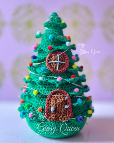 Grüner gehäkelter Weihnachtsbaum mit farbigen Pompons, feiner Lichterkette und runden sowie bogenförmigen Applikationen.
