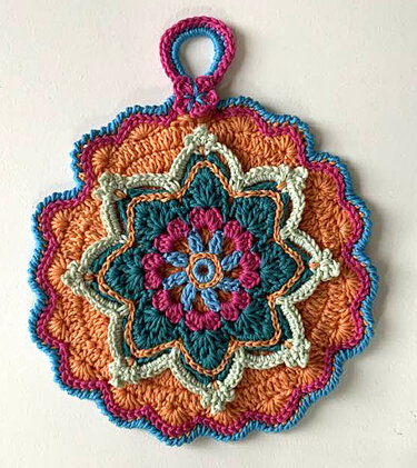 Runder, bunter, handgehäkelter Topflappen mit komplexem Mandala‑Muster in Orange, Türkis, Pink und Hellblau, mit Aufhängeschlaufe