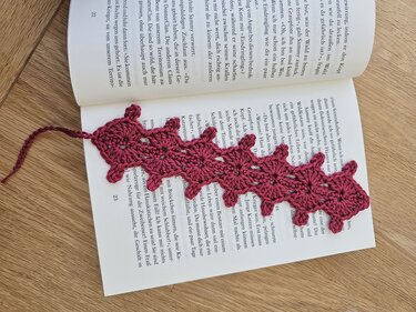Gehäkeltes Lesezeichen in Dunkelrosa im Raupenmuster in geöffnetem Buch