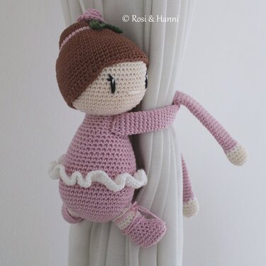 Gehäkelte Puppe mit langen Armen und Rüschen, die einen Vorhang hält