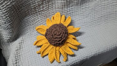 Gehäkelte Sonnenblume in Gelb und Braun auf hellgrauem Stoff