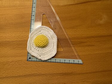 Kleines gehäkeltes Spiegelei auf transparentem Geodreieck zur Größendarstellung