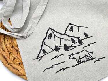 Schwarze Linienzeichnung von Bergen, Tannen und einer weidenden Kuh auf hellgrauer Stofftasche