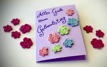Lila Geburtstagskarte mit gehäkelten Blumen in Rosa, Grün, Blau und Magenta