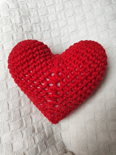 Rotes gehäkeltes Amigurumi-Herz auf weißem, strukturiertem Stoff