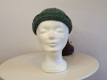 Dunkelgrün‑lila gestrickte Mütze auf neutralem Schaufensterkopf