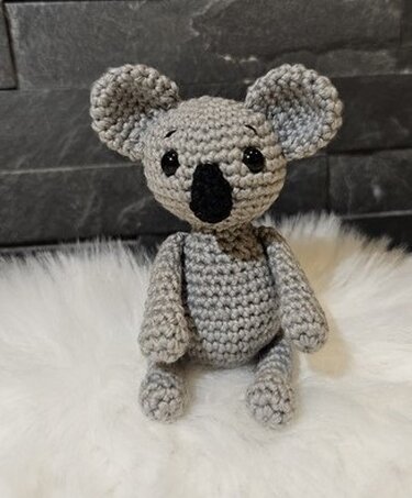 Gehäkelter grauer Koala Amigurumi sitzend auf weißem Fell