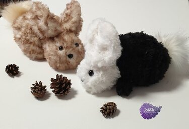 Zwei flauschige Hasen, braun und schwarz-weiß, mit Tannenzapfen.