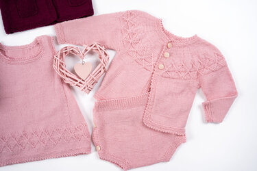 Rosa gestricktes Baby-Set mit Jacke, Strampler und ärmellosem Oberteil, feines Ajourmuster und geflochtenes Herz als Dekoration auf hellem Hintergrund