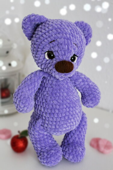Fertiger flauschiger lila Amigurumi-Teddyb mit dunklen Augen und brauner Nase.