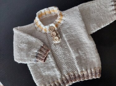 Beiger gestrickter Baby-Pullover mit drei Holzknöpfen und dezenten Streifen an Kragen und Bündchen