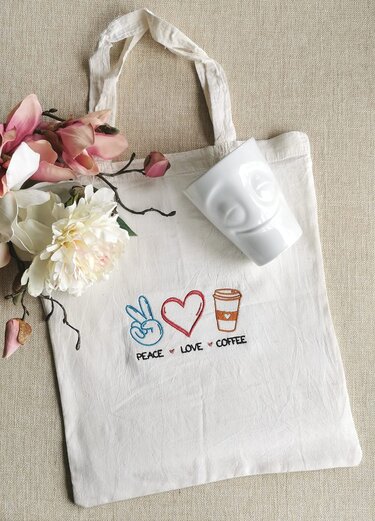 Helle Stofftasche mit besticktem Friedenszeichen, Herz, Kaffeebecher und dem Schriftzug 'Peace Love Coffee'.