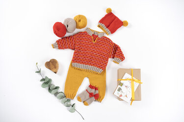 Gestricktes Babyset: roter Pullover, senfgelbe Hose, Mütze mit Bommel, kleine Socken, Garnknäuel und Geschenkbox