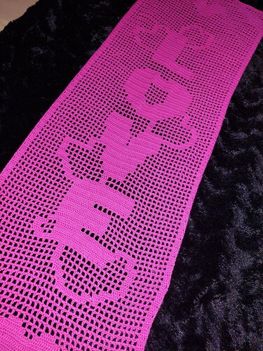 Magenta gehäkelter Tischläufer im Filetmuster mit LOVE-Schriftzug und Herz-O auf dunklem Hintergrund