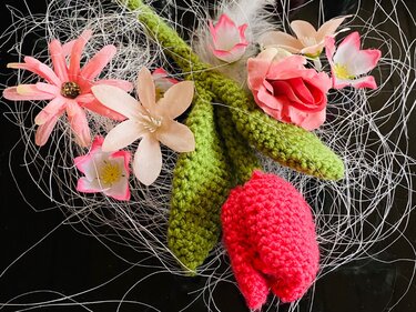 rote gehäkelte Tulpe mit zwei grünen Blättern und rosa Dekoblumen auf schwarzem Hintergrund