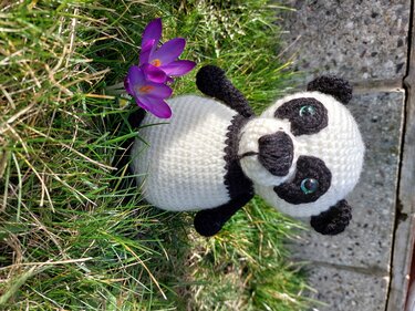 Gehäkelter schwarz-weißer Amigurumi-Panda auf Gras neben violettem Krokus
