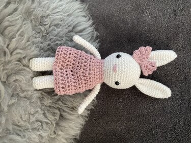 Weißer gehäkelter Amigurumi-Hase mit rosa Kleid und Ohrschleife, liegend