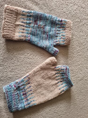 Paar gestrickter fingerloser Handschuhe in Beige mit blauen, türkisen und violetten Akzenten auf hellem Untergrund.