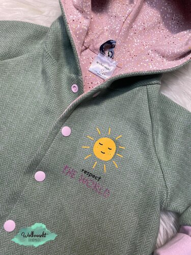 Pastellgrüne Kapuzenjacke mit rosa Innenfutter und gelbem Sonnenplott auf der Brust